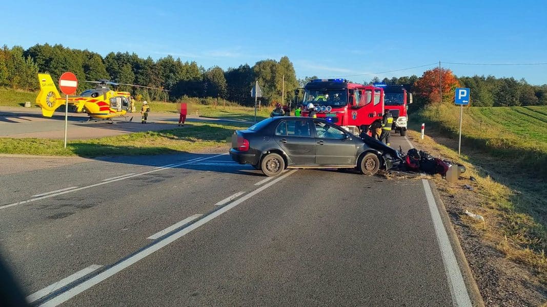 Wypadek na drodze krajowej z udziałem motocykla i samochodu, na miejscu straż pożarna i śmigłowiec LPR.