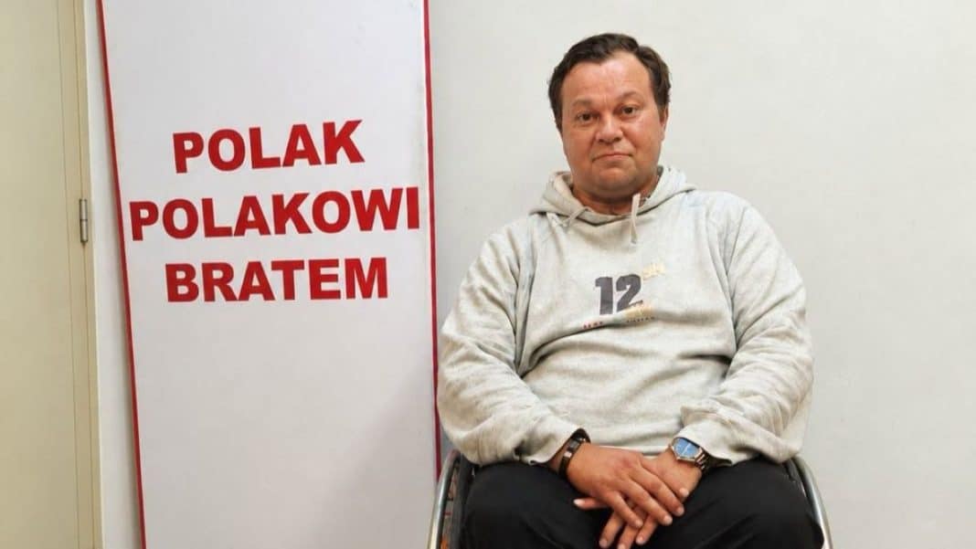 Mężczyzna na wózku inwalidzkim siedzi w pomieszczeniu obok plakatu z napisem