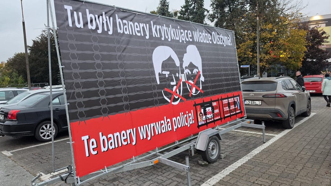 Baner krytykujący władze Olsztyna z wizerunkami prezydenta i jego zastępczyni, z czerwonymi krzyżami i hasłem.