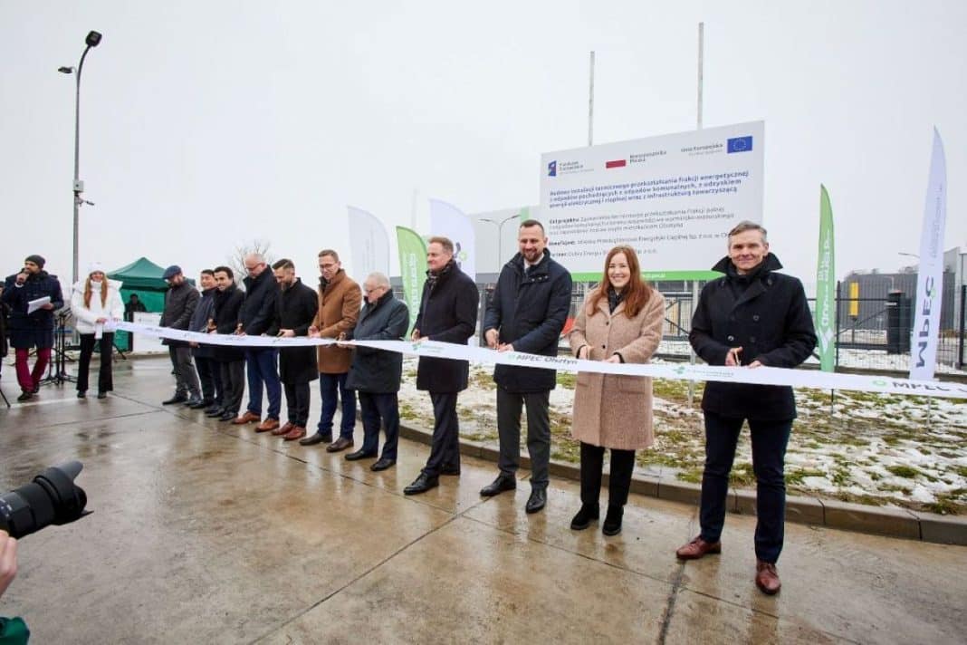 Grupa osób podczas uroczystości otwarcia spalarni odpadów w Olsztynie, na tle tablicy informacyjnej.