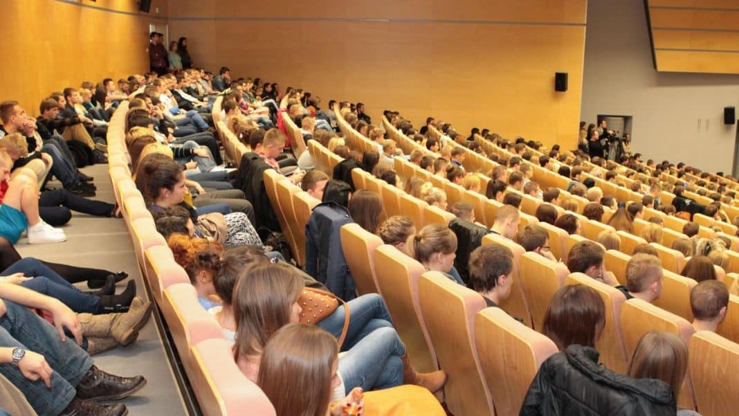Sala wykładowa wypełniona studentami siedzącymi na krzesłach, słuchającymi wykładu lub prezentacji.