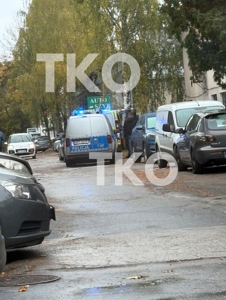 Zdjęcie przedstawia policję i samochody na ulicy, obok widać maczetę wbita w ziemię.